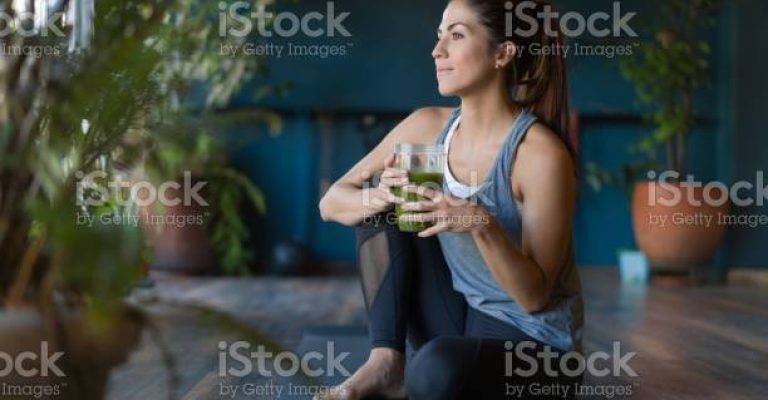 Portrait of a fit Latin American woman drinking a green detox smoothie at the gym - healthy lifestyle concepts