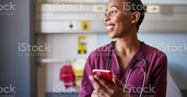 Smiling female nurse using smart phone. Medical professional is wearing uniform. She is looking away at hospital.